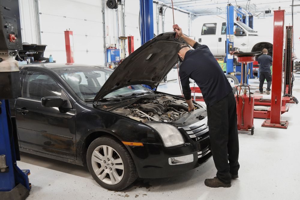 Car Maintenance in Steeleville IL At Mevert Automotive. Auto technician standing under the open hood of a black Ford Fusion inside a service bay
