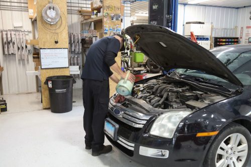 A Mevert Automotive technician working under the hood of a Ford car.